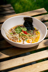 in a restaurant on the street on wooden table a white plate with Japanese udon soup with egg and...