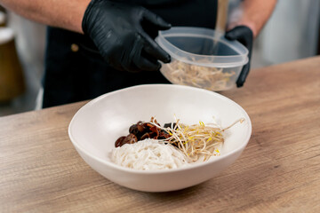 fast food establishment large chef in a black uniform prepares Japanese udon soup from previously...