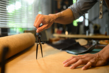 Close up of craftsman hands meticulously measuring a piece of leather using a pair of dividers in...