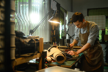 Professional male artisan using a hammer and other tools to shape and detail the leather piece in the workshop