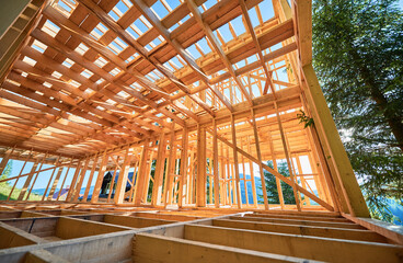 Under-construction residential wooden frame home located near a forest. Commencement of a new construction project for a cozy house or a mountain cottage. Idea of contemporary ecological construction.