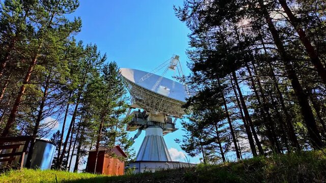 Exterior view of the Irbene radio telescope standing tall amidst deep woodland, highlighting its massive structure and technological significance