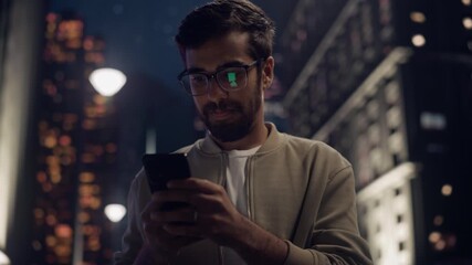 Man in a Casual Coat Using Smartphone on a Street at Night, Surrounded by City Lights. Young Arab Male Engaging With Social Media, Chatting With Friends, Enjoying Vibrant Urban Atmosphere - Powered by Adobe