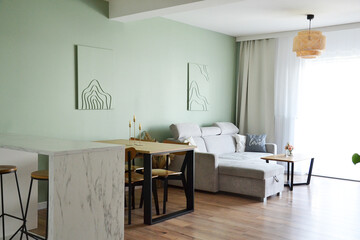 Przytulny salon jadalnia z miętową zieloną ścianą obrazami i wygodną szarą sofą i zasłonami i firaną i sztuką line art