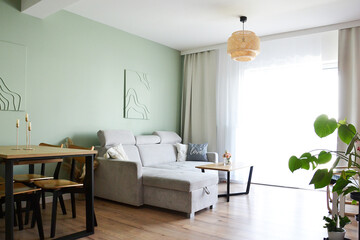 Przytulny salon jadalnia z miętową zieloną ścianą obrazami i wygodną szarą sofą i zasłonami i firaną i sztuką line art © VILKTERIO