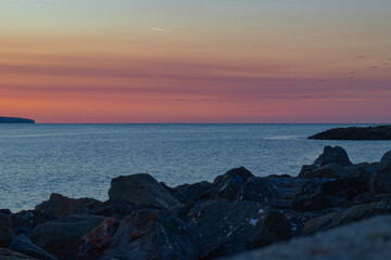 calm on the sea before dawn, stones on the shore and colorful sky waiting for the first rays of the sun