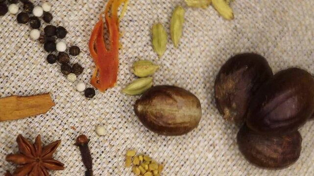 Close up Indian Spices Rotate on Slow motion. Scattered spices mix cardamom, Jhaifal, star anise, Javitri, cinnamon, cloves, methi , black and white pepper.  Backgrounds, texture.