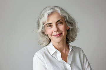 Fototapeta premium The photograph captures an older woman with lovely gray hair, radiating confidence and happiness through a serene smile. She looks elegant in a white shirt, embodying calm and charm