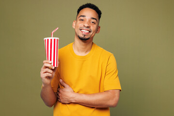 Young man of African American ethnicity wears yellow t-shirt casual clothes hold in hand cup of soda pop cola fizzy water isolated on plain pastel green background studio portrait. Lifestyle concept.