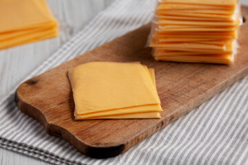 Yellow Cheddar American Cheese Stacked Slices on a wooden board, side view.