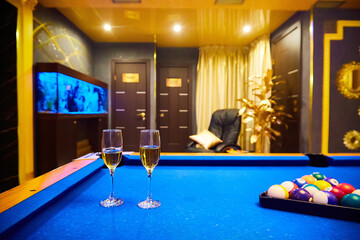 Two glasses of champagne rest on a blue pool table in a dimly lit game room