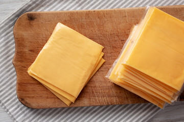 Yellow Cheddar American Cheese Stacked Slices on a wooden board, top view.