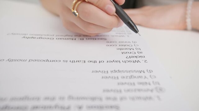 Female circles correct answers in standard geography exam test paper with pen. Student filling up the answer sheet, choosing right answer, close up shot.