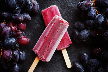 Two berry-grape popsicles next to clusters of dark grapes on a dark background