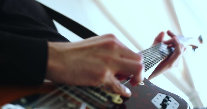 Beautiful slow motion detail shot of hands playing an instrumental solo on electric guitar in a recording studio with natural light coming in from the balcony.