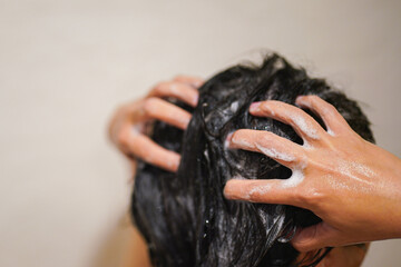 A black hair woman is washing hair with shampoo and conditioner during taking rain shower. Healthcare activity scene, Close-up from the back.