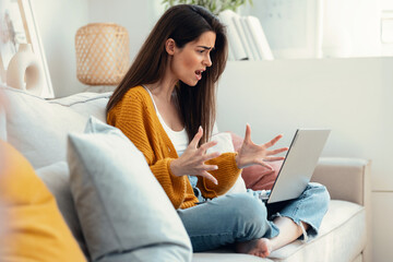 Worried angry woman having problems while doing a videocall with laptop sitting on couch at home