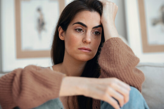Depressed young woman overthinking while sitting on the couch at home
