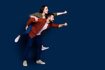 Profile side photo of cheerful couple wear stylish clothes fly air have fun play look empty space isolated on dark blue color background