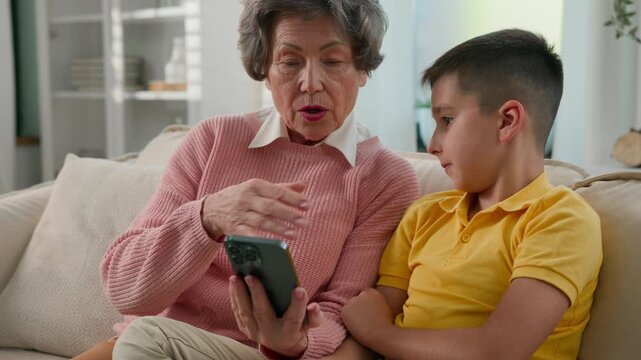 Caucasian grandmother grandson enjoying time together on couch home old woman grandma kid boy grandchild using mobile phone shopping in online store teaching learning modern technology on smartphone