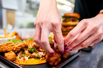 Close-up of hands with purple nail polish placing fried chicken pieces on a tray with various other foods
