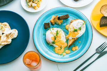 Eggs, Benedict on bread toast and avocado on a slice of rye bread, cheese and a glass of orange juice on the table. Selected focus.