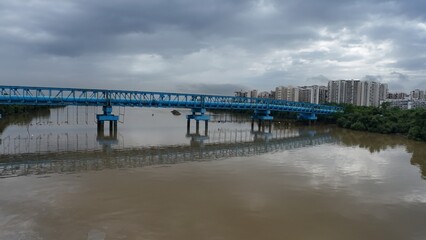 A blue-colored pipeline bridge over a river, with water beneath and a cloudy sky, emphasizing its architectural structure.
