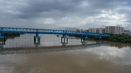 Obraz premium A blue-colored pipeline bridge over a river, with water beneath and a cloudy sky, emphasizing its architectural structure. 