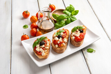 Bruschette con pomodoro fresco, mozzarella, olive, basilico e olio extravergine di oliva, spuntino italiano, dieta mediterranea 