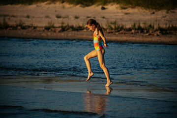 A girl in a colorful swimsuit playing energetically in the ocean waves, capturing a moment of joy and movement by the sea. The image emphasizes the fun and excitement of a summer day at the beach