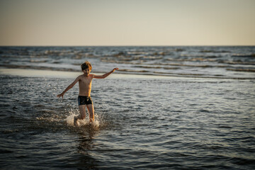 Fototapeta premium A boy energetically splashing in the ocean waves, creating a burst of water droplets around him. The image captures the fun and excitement of a day at the beach, with the boy enjoying the summer sun