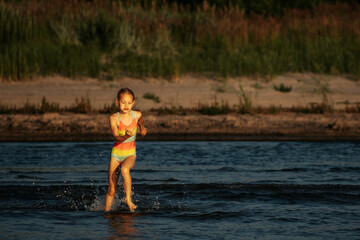Fototapeta premium A girl in a colorful swimsuit playing energetically in the ocean waves, capturing a moment of joy and movement by the sea. The image emphasizes the fun and excitement of a summer day at the beach