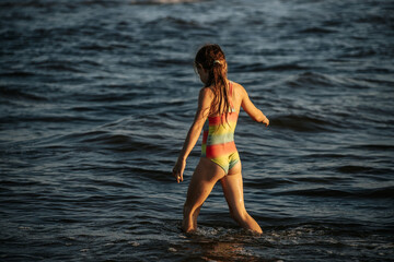 Fototapeta premium A girl in a colorful swimsuit playing energetically in the ocean waves, capturing a moment of joy and movement by the sea. The image emphasizes the fun and excitement of a summer day at the beach