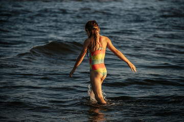 Fototapeta premium A girl in a colorful swimsuit playing energetically in the ocean waves, capturing a moment of joy and movement by the sea. The image emphasizes the fun and excitement of a summer day at the beach