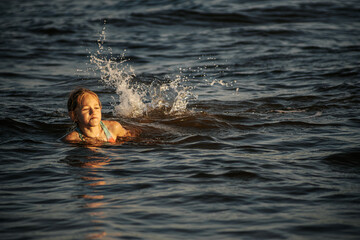 Fototapeta premium A girl in a colorful swimsuit swimming in the ocean waves, enjoying the water and the summer day. The image captures her playful and energetic moment in the sea