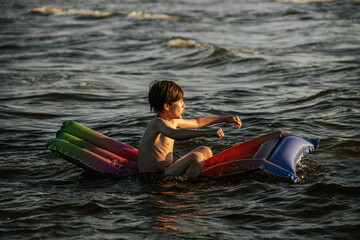Obraz premium A boy riding an inflatable raft in the waves at the beach, capturing a moment of fun and adventure in the water. The image shows his determination and enjoyment as he navigates the waves.