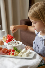 Cute little girl having breakfast, cereals with yogurt, tasty and healthy choice between various dishes served on the table