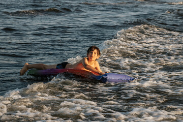 A boy riding an inflatable raft in the waves at the beach, capturing a moment of fun and adventure in the water. The image shows his determination and enjoyment as he navigates the waves.