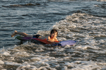 A boy riding an inflatable raft in the waves at the beach, capturing a moment of fun and adventure in the water. The image shows his determination and enjoyment as he navigates the waves.