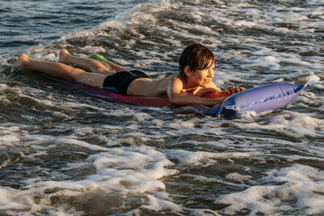 A boy riding an inflatable raft in the waves at the beach, capturing a moment of fun and adventure in the water. The image shows his determination and enjoyment as he navigates the waves.