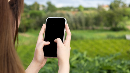 Close up of a business woman's hand holding and using a smartphone with a blank black screen to display your graphics.
