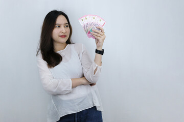 Beautiful Asian young woman holding cash money in Indonesian rupiah and looking up thoughtful