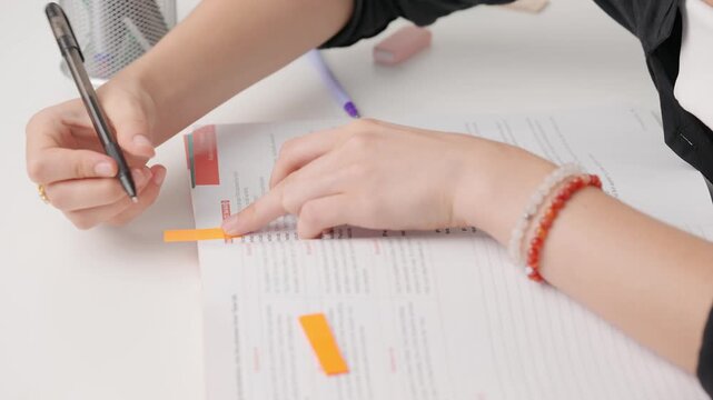 Female making bookmarks in standard exam test paper book with colorful tape. Student placing sticking tape tab for bookmarks in working journal.