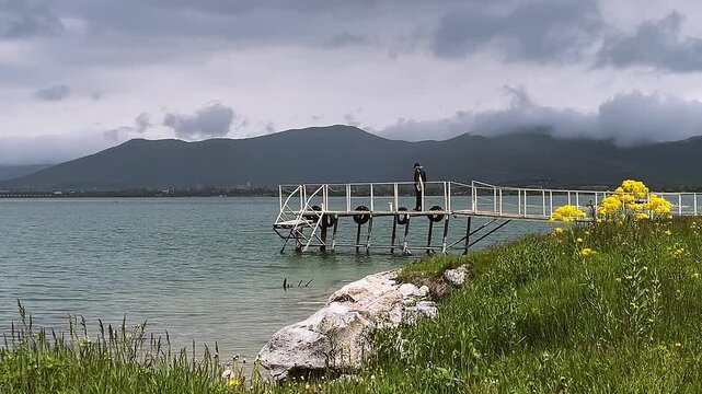 Man on peaceful lakeside pier with mountains in background. Sevan lake, Armenia