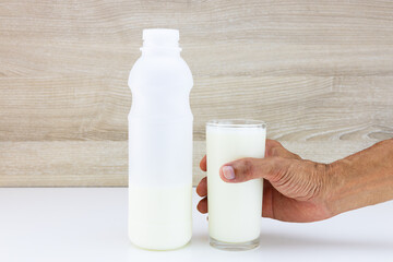 Hand holding glass of fresh milk on blurred wooden wall background