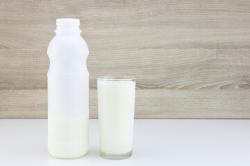 Glass of fresh milk and bottle of milk on blurred wooden wall background