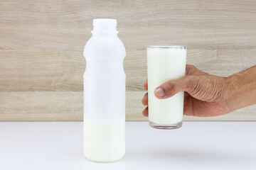 Hand holding glass of fresh milk on blurred wooden wall background
