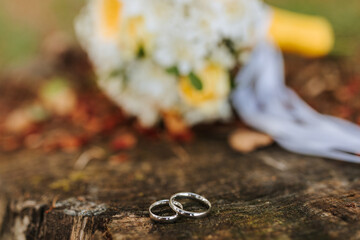 Two wedding rings are on a wooden surface. The rings are silver and are placed next to a bouquet of white flowers. Concept of love and commitment, as the rings symbolize the bond between two people