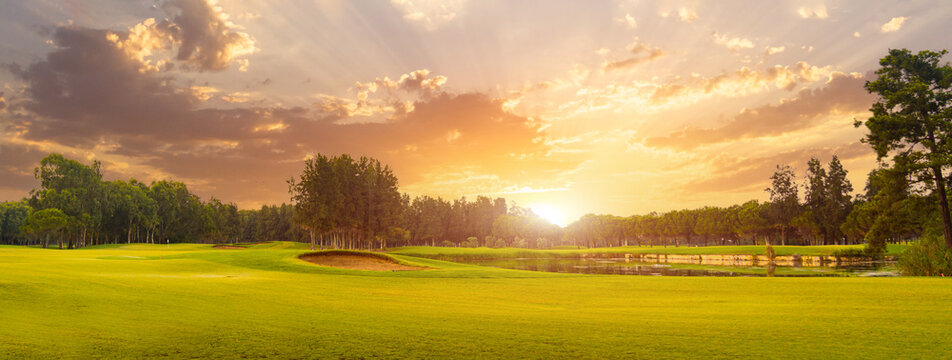 Golf course at sunset with beautiful sky and sand trap. Scenic panoramic view of golf fairway with bunker. Golf field with pines