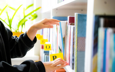 Girl choosing books on shelves in the light school library